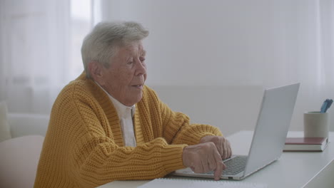 elderly-Woman-are-using-laptop-to-make-video-call-talking-gesturing-showing-thumbs-up-hand-gesture-indoors.-Old-woman-and-modern-devices-concept.